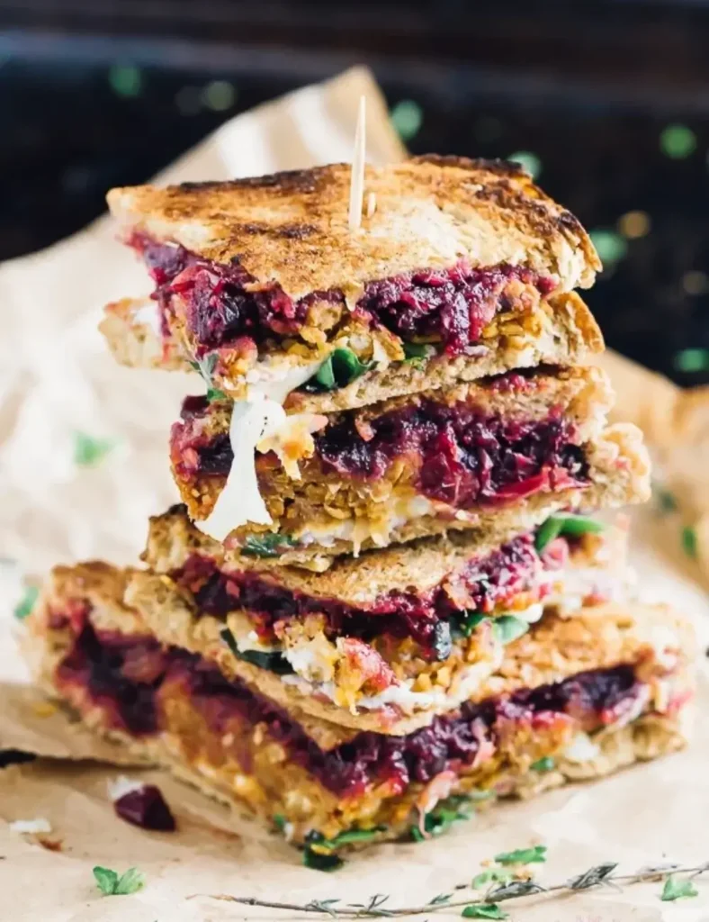 Grilled vegan meatloaf and cranberry leftover sandwich sliced in half on a wooden board