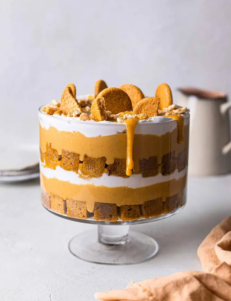 Layered vegan pumpkin trifle in a glass bowl showing cake, custard, cream and ginger cookies
