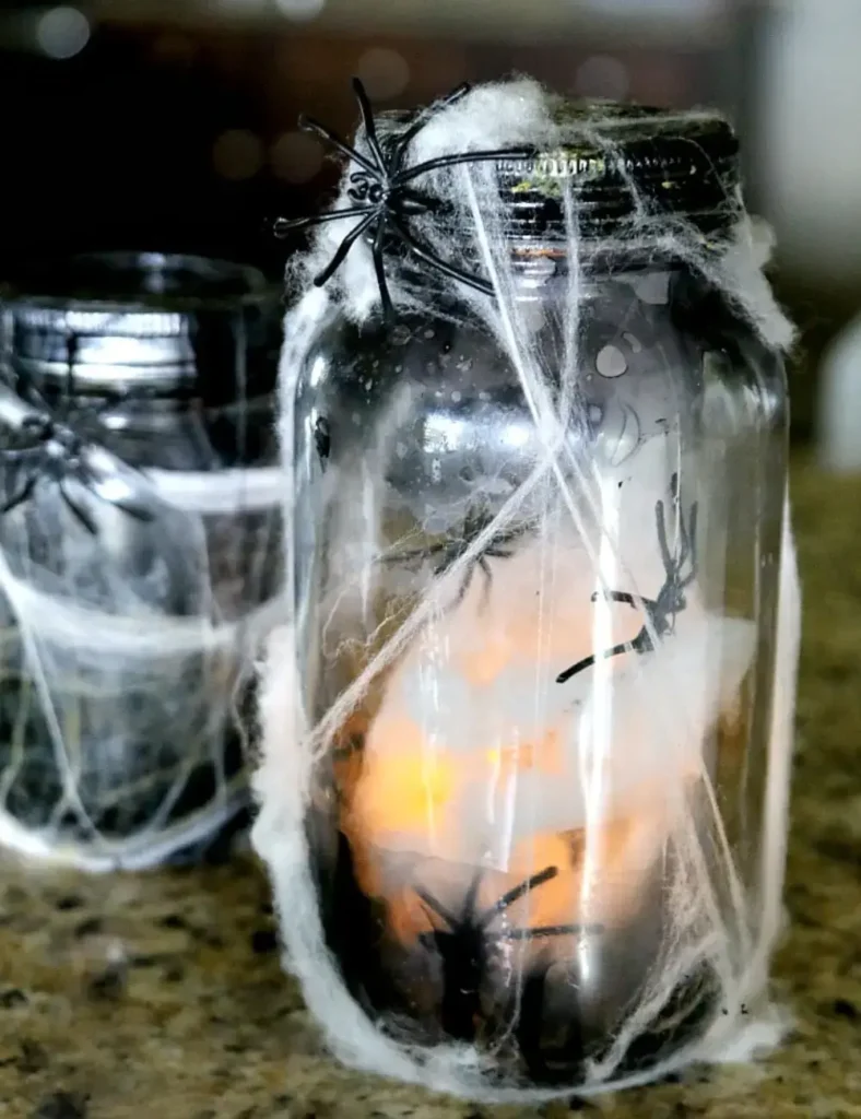 Light-up spider mason jar craft with aged black-tinted glass, fake spiderweb and a glowing tea light inside
