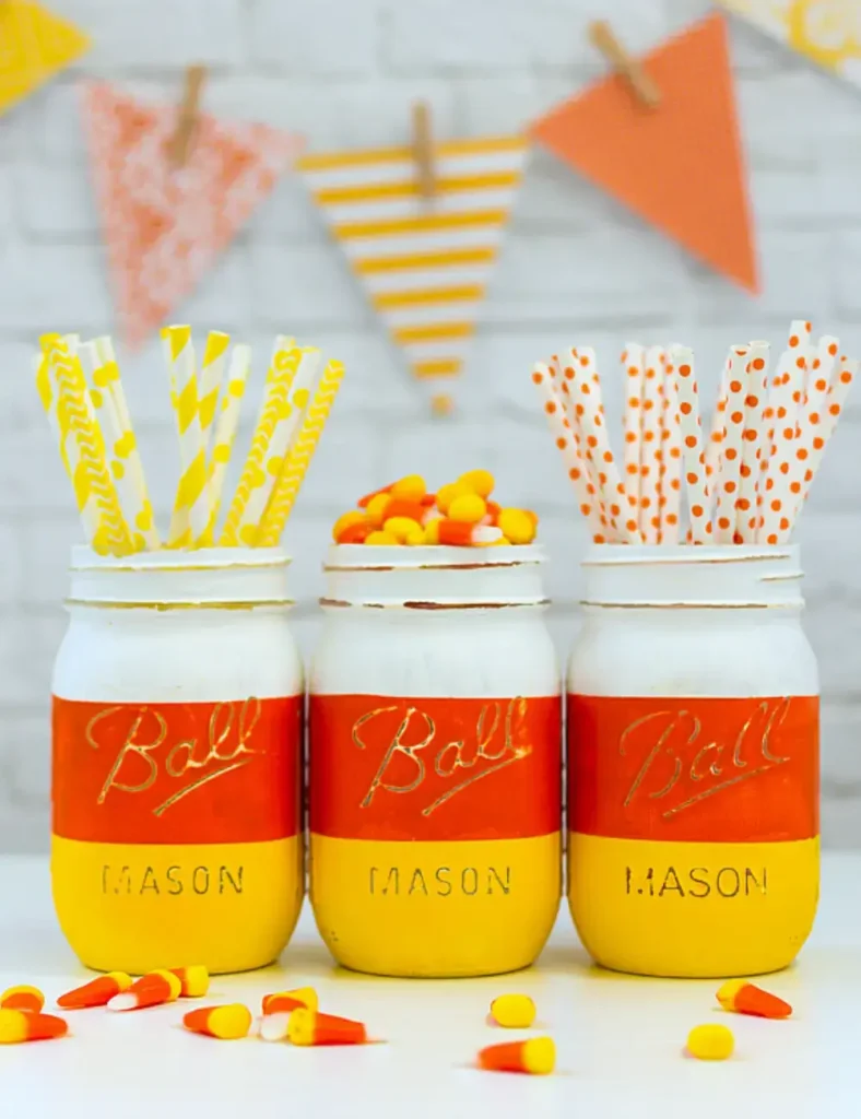 Mason jar painted in white, yellow and orange stripes to resemble a giant candy corn