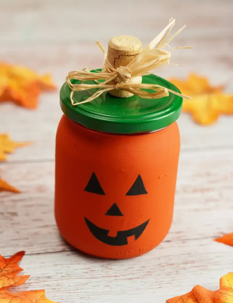 Mason jar painted orange with a hand-painted jack-o-lantern face and a raffia bow topped lid