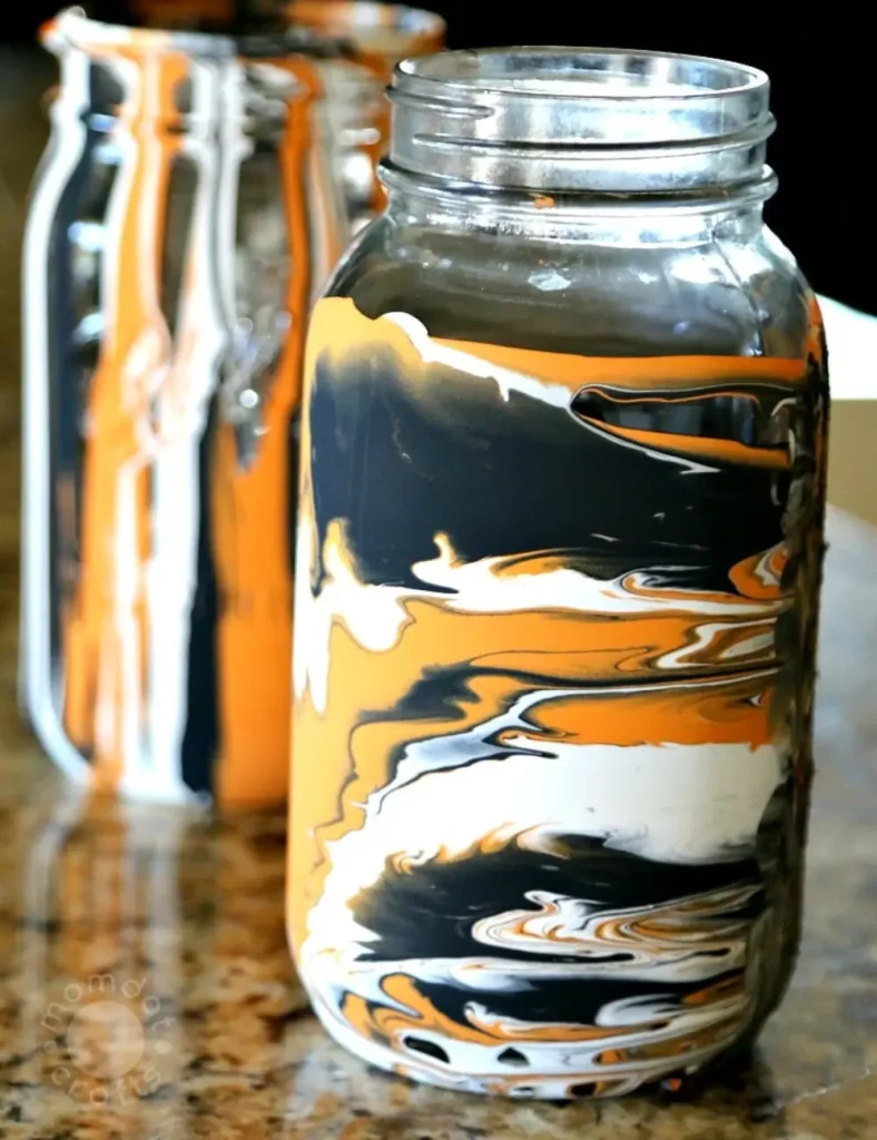 Mason jar with orange, black and purple drip-painted design in an abstract marbled pattern