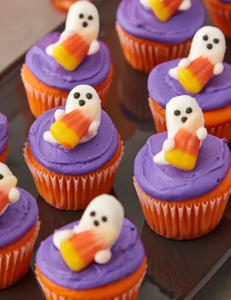 Mini cupcakes with purple frosting topped with ghost and candy corn decorations