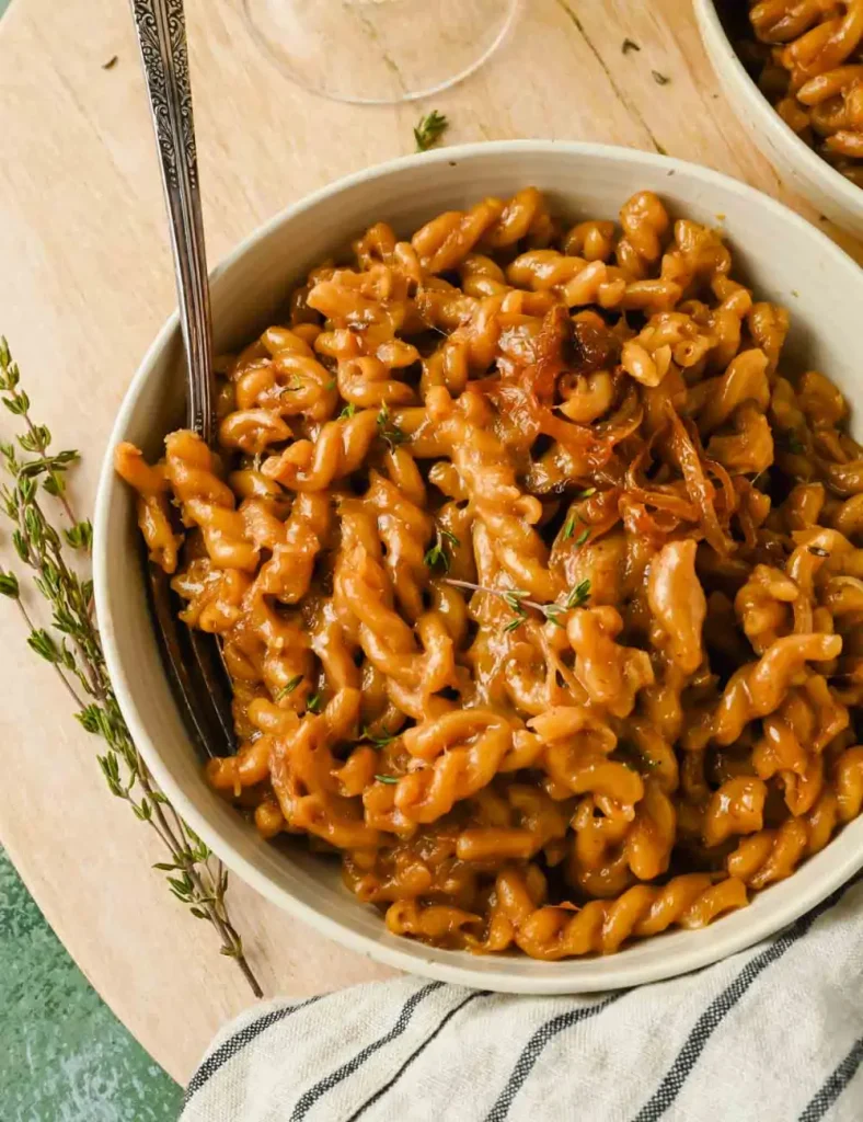 One pot French onion pasta in a white bowl topped with caramelized onions, melted Gruyère and fresh thyme