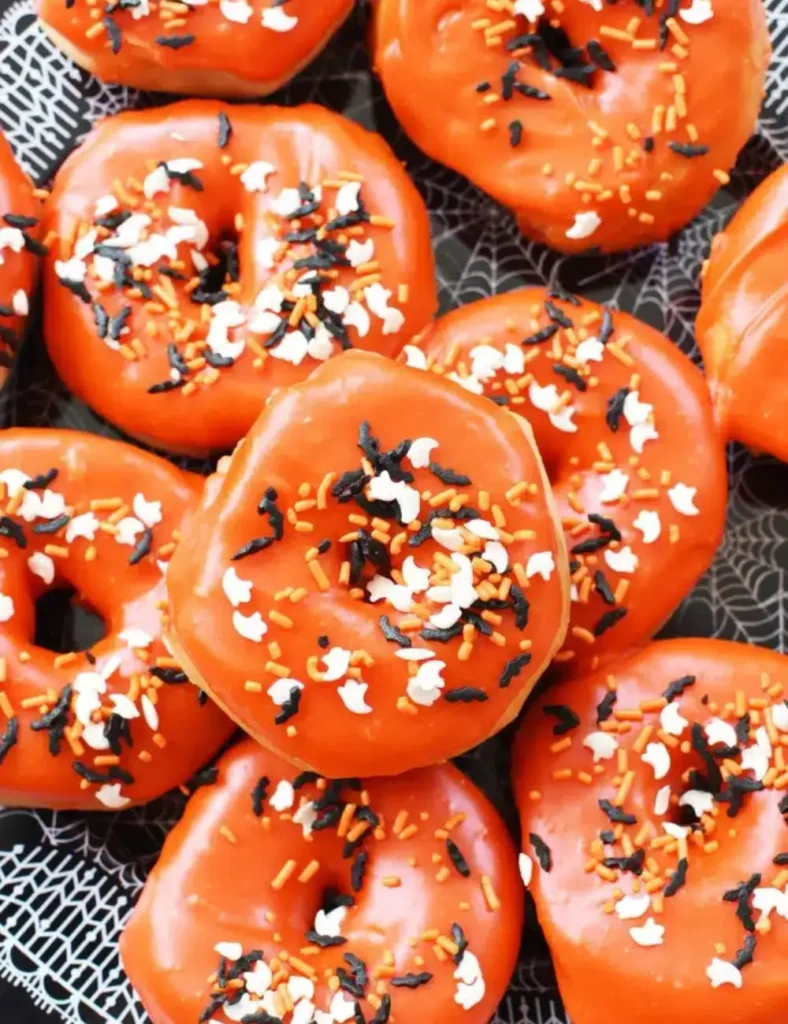 Orange glazed donuts topped with Halloween sprinkles cooling on a wire rack
