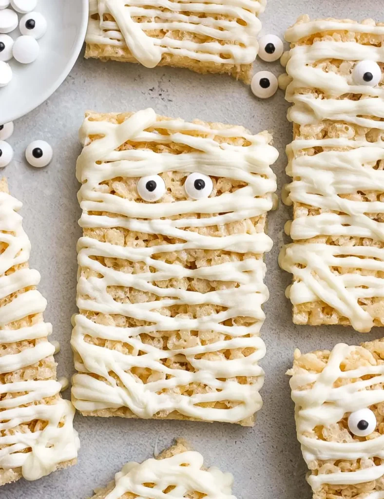 Rice Krispie treats decorated with white chocolate drizzle and candy eyes to look like mummies