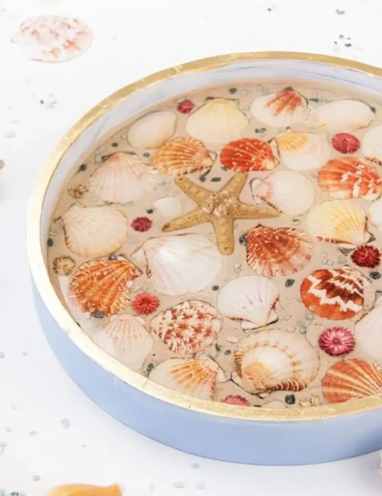 Round wooden serving tray with seashells set in a resin, sand-look finish