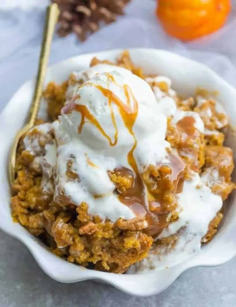 Serving of pumpkin cobbler in a bowl topped with vanilla ice cream and caramel sauce