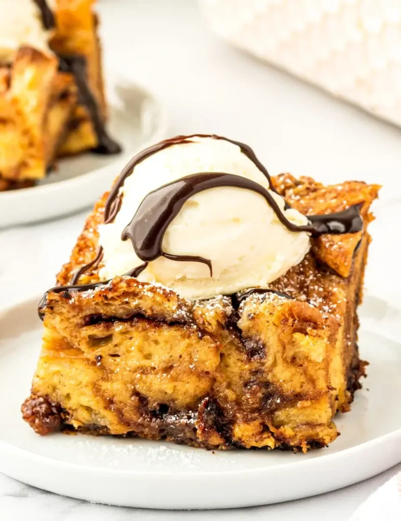 Slice of Nutella croissant bread pudding on a plate with vanilla ice cream and chocolate sauce