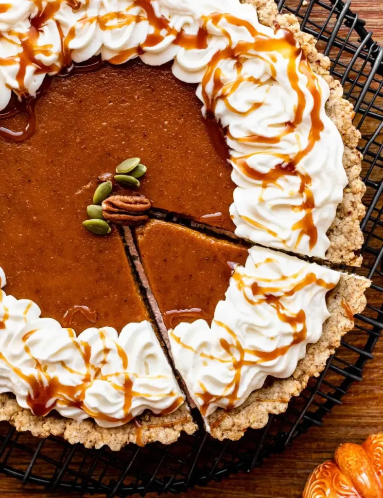 Slice of spiced pumpkin tart with pecan crust, topped with whipped cream and salted caramel