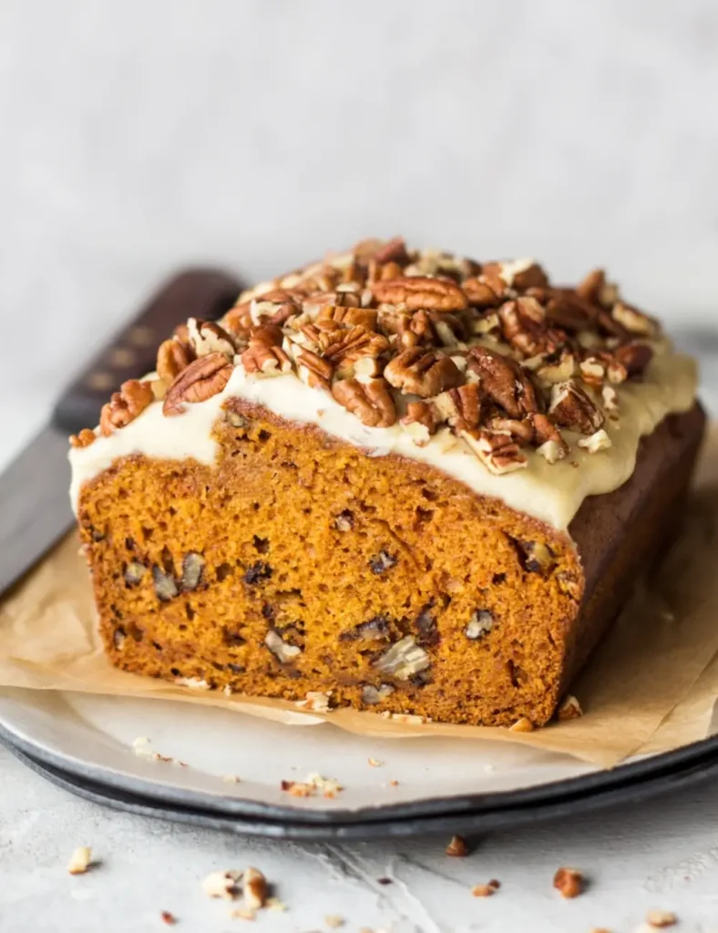 Sliced vegan pumpkin bread with maple cashew frosting and chopped pecans on top