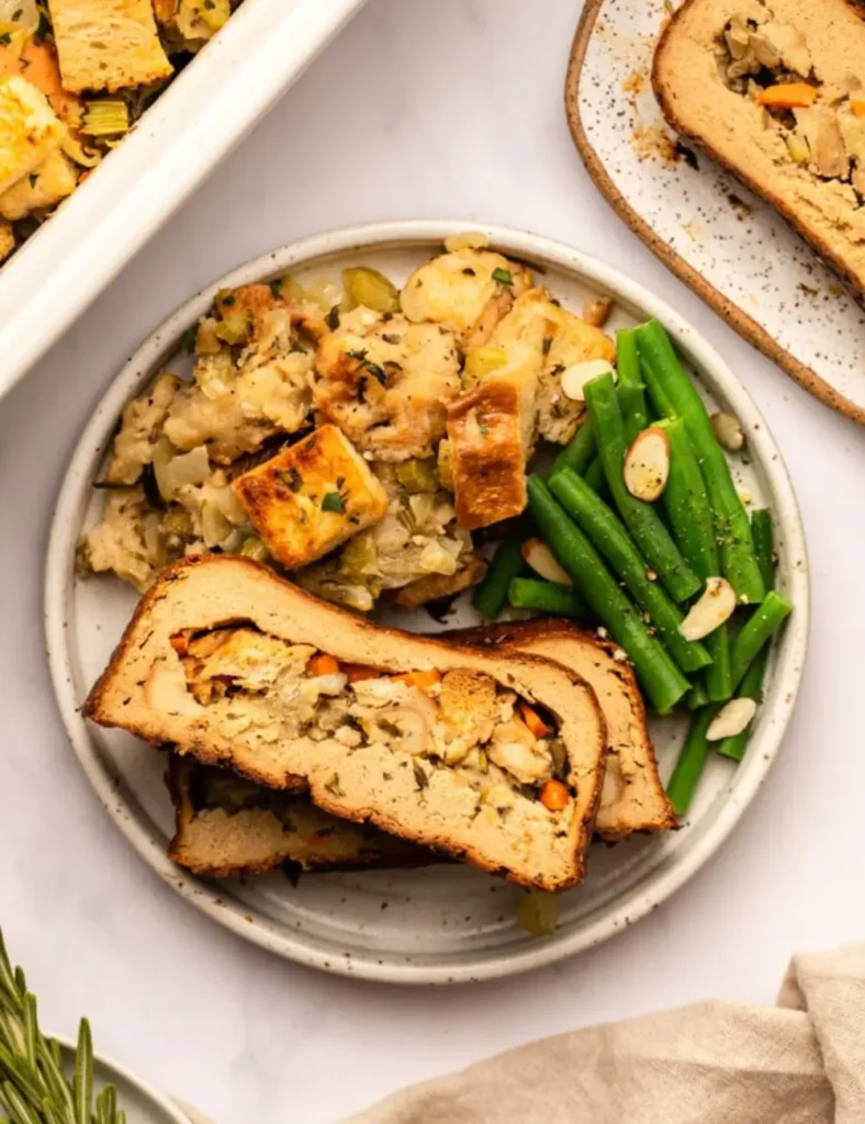 Sliced vegan tofu turkey loaf showing the stuffing center, served with green beans and roasted vegetables