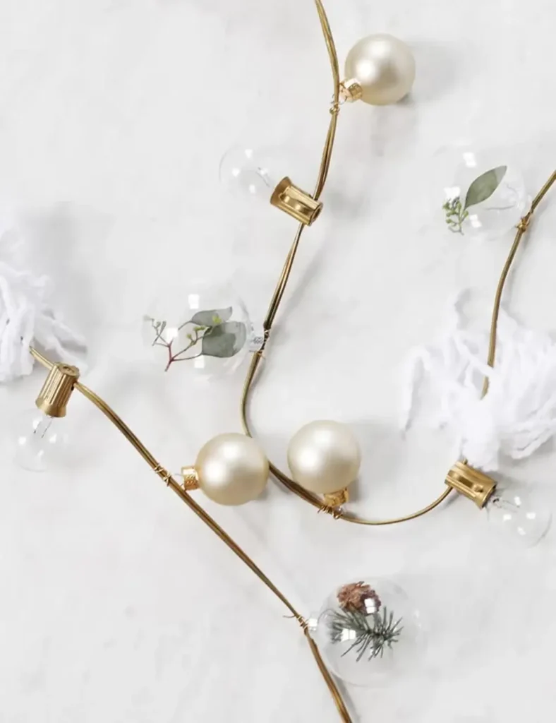 String lights decorated with yarn tassels and greenery-filled clear ornaments