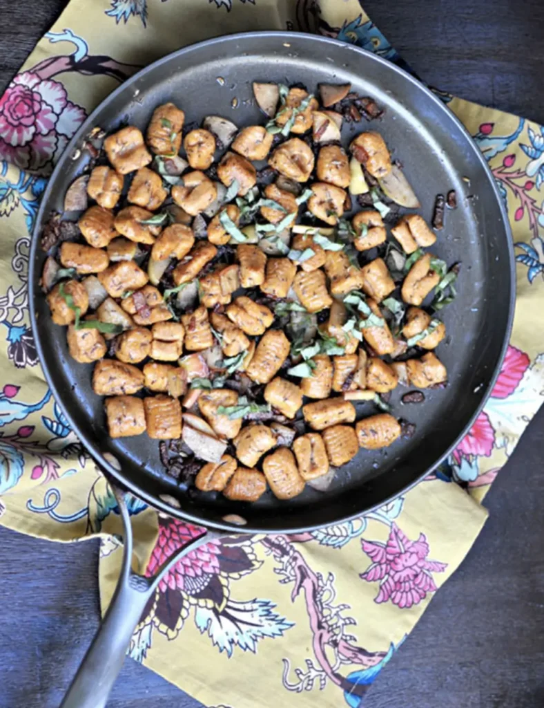 Sweet potato gnocchi with sliced apple, crispy bacon and balsamic in a shallow bowl