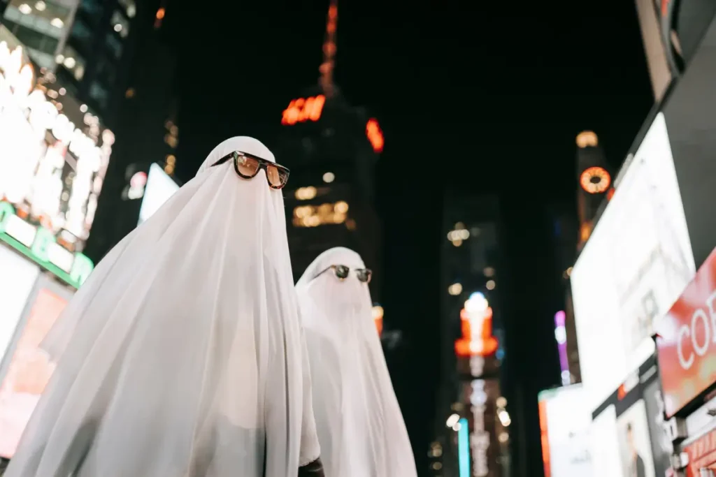 Two people in spooky ghost costumes with sunglasses on city street at night