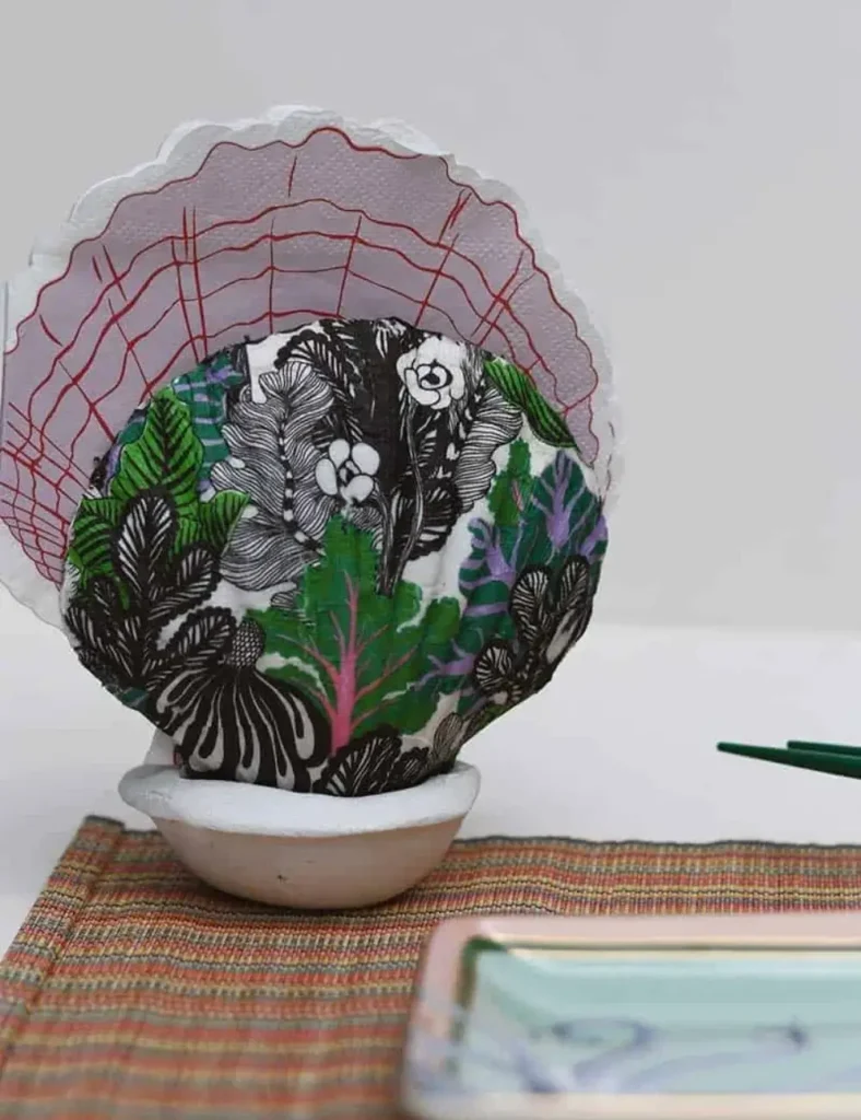 Two scallop shells set upright in a clay base, holding folded napkins