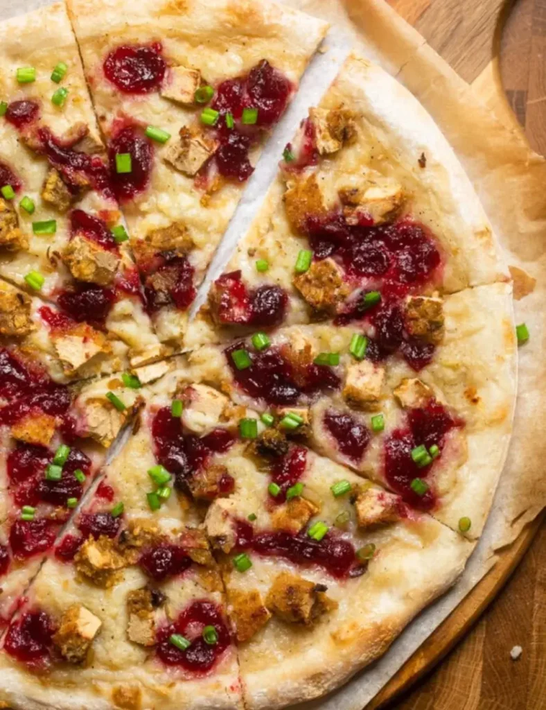 Vegan Thanksgiving leftover pizza topped with mashed potato, cranberry sauce and vegan turkey, sliced on a board
