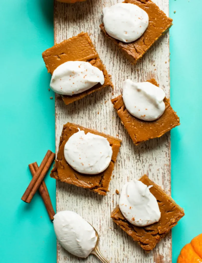 Vegan gluten-free pumpkin pie bars topped with coconut whipped cream on a wooden board