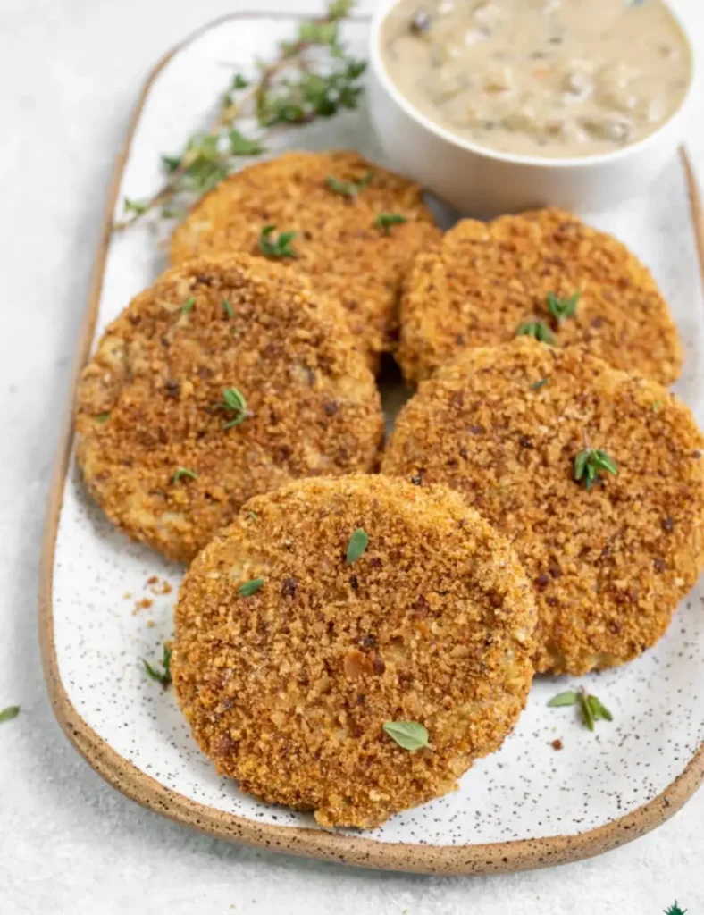 Vegan leftover mashed potato cakes coated in stuffing crumbs, stacked on a plate with mushroom gravy