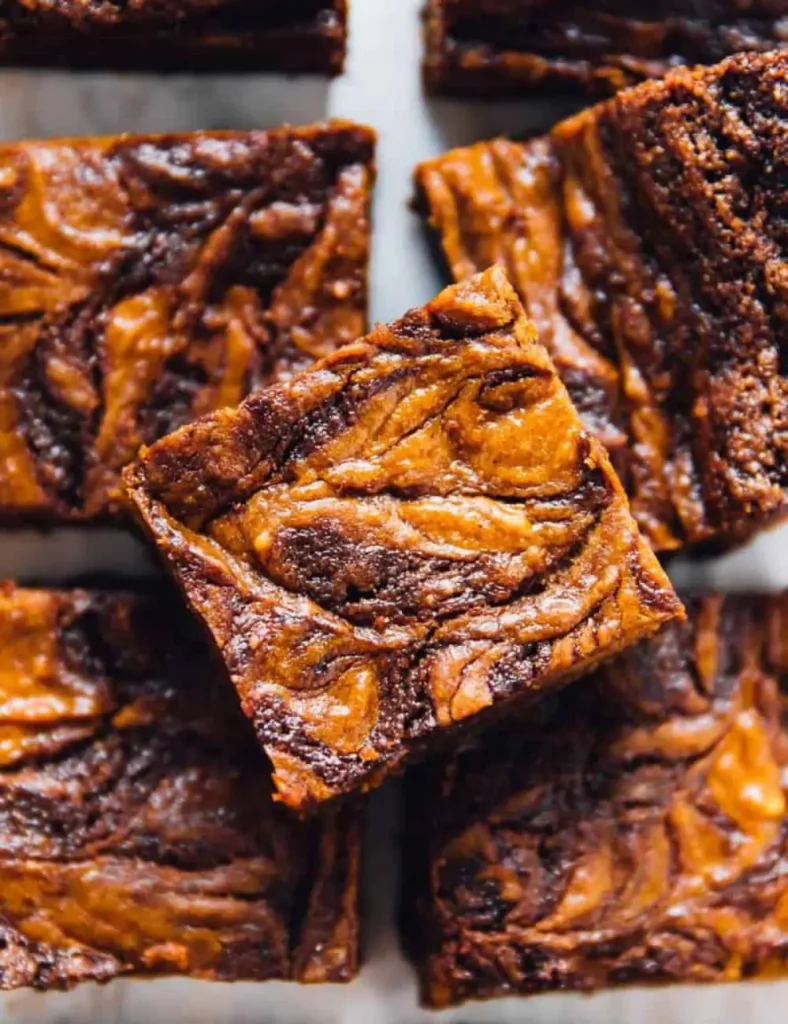 Vegan pumpkin cheesecake swirl brownies stacked, showing marbled pumpkin and chocolate