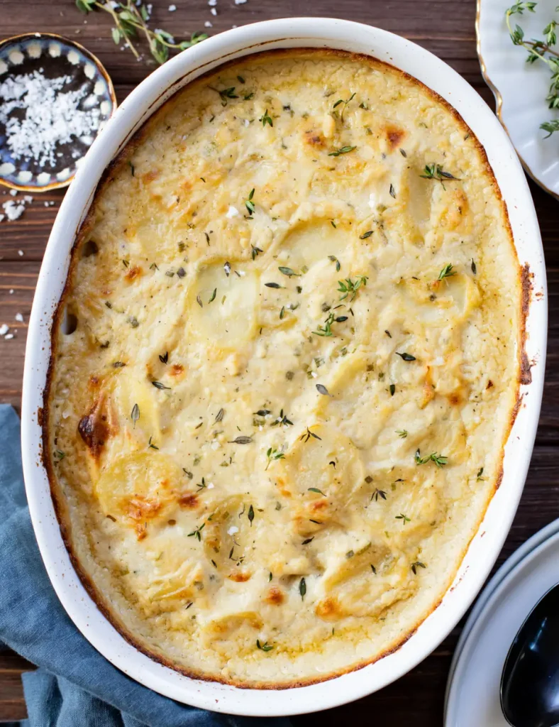 Vegan scalloped potatoes in a baking dish with layered potato slices, crispy top and fresh thyme