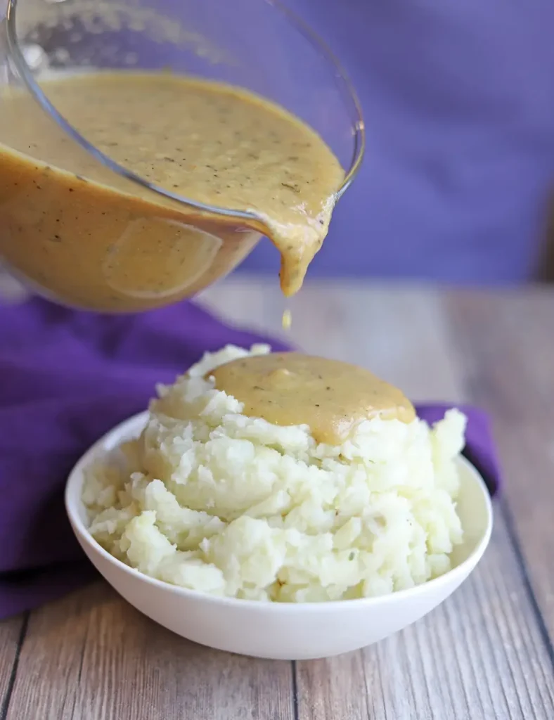 Vegan turkey gravy being poured from a gravy boat over a bowl of creamy mashed potatoes
