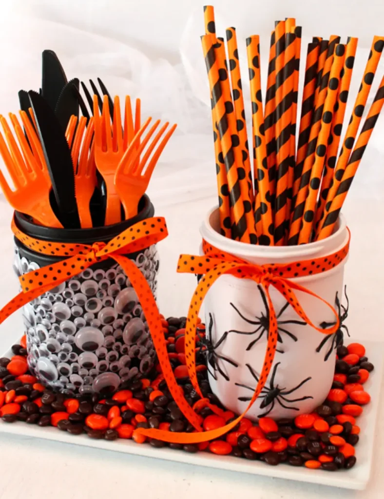 White mason jar decorated with glued-on plastic spiders and a Halloween ribbon, used as a party table holder