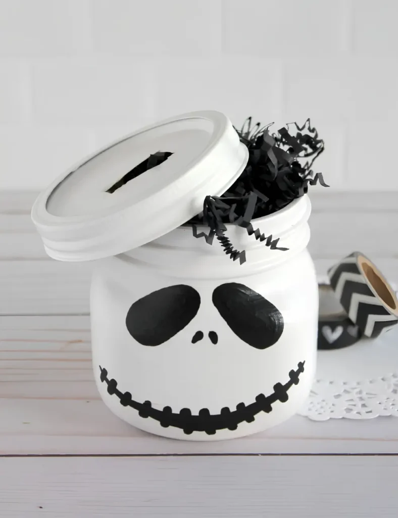 White mason jar painted with a skeleton face, used as a Halloween-themed piggy bank