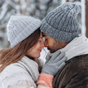 A couple shares an intimate moment in a snowy forest, embracing warmth and love.