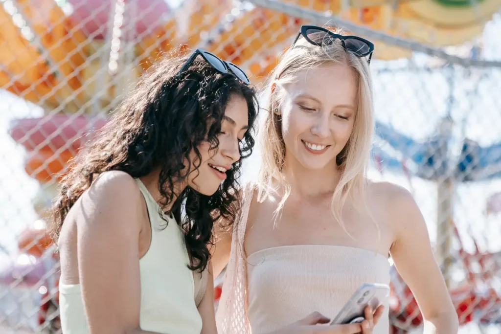 Two young women having fun and taking photos at a sunny carnival.