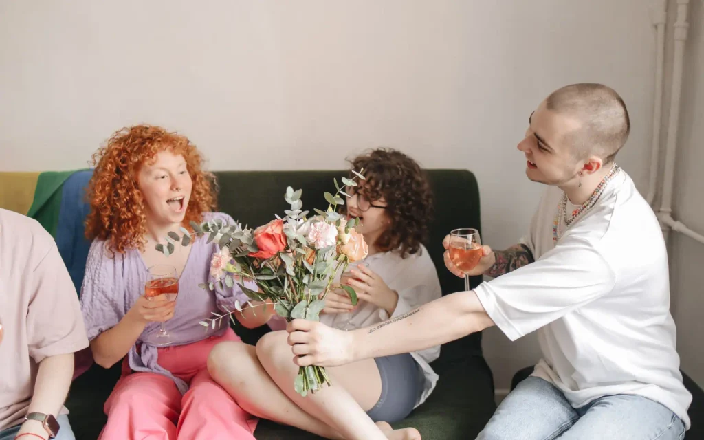 A group of friends enjoying a cheerful moment with flowers and drinks indoors.