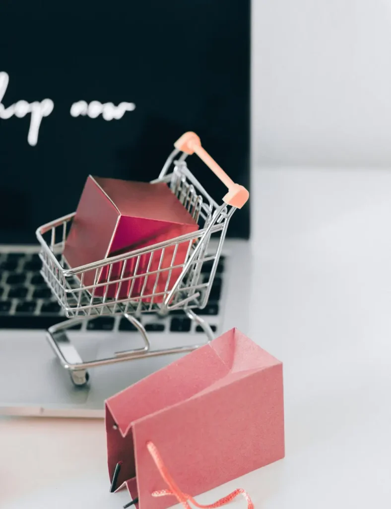 A miniature shopping cart with a parcel on a laptop symbolizes online shopping and e-commerce