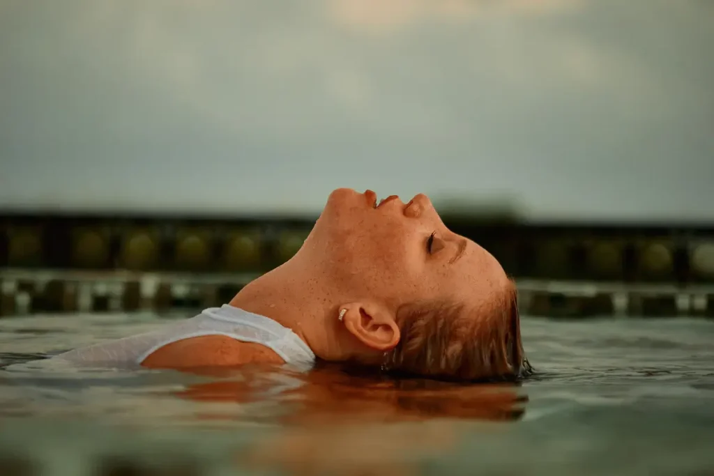 A serene moment of a woman peacefully floating in a pool during sunset, eyes closed and relaxed.