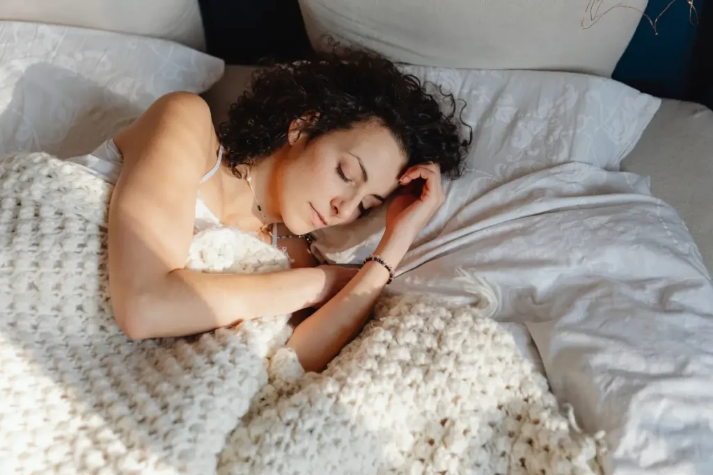 A woman peacefully sleeping on a bed with white bedding under natural light