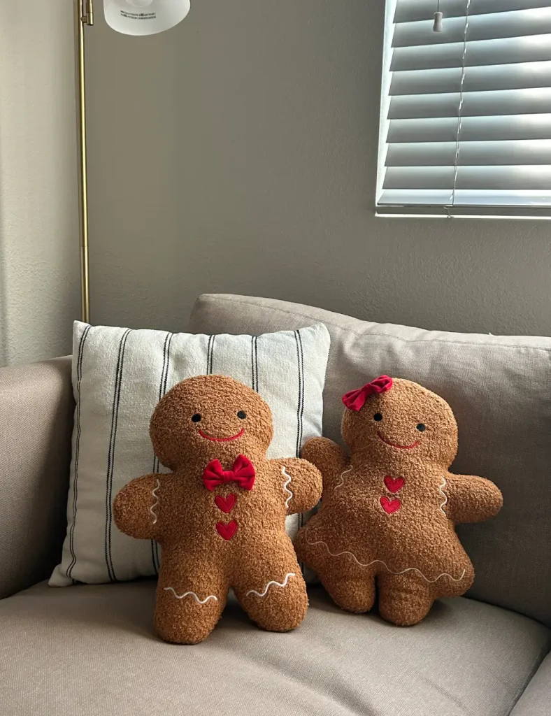 Boucle gingerbread man and woman pillows with red bows on a beige sofa