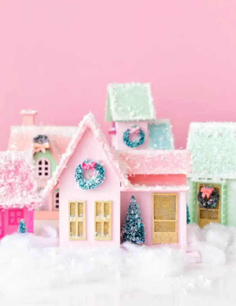 Brightly painted birdhouse Christmas village with glittery snow roofs, mini wreaths and small trees on a mantel