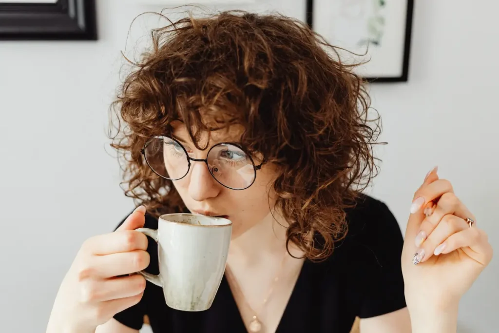 Caucasian woman with curly hair and glasses enjoying coffee indoors