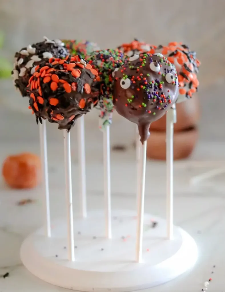 Chocolate-dipped donut hole Halloween cake pops covered in sprinkles, on lollipop sticks