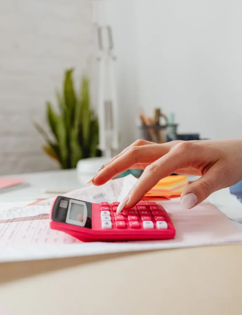 Close-up of a hand pressing buttons on a pink calculator on a desk, indoors