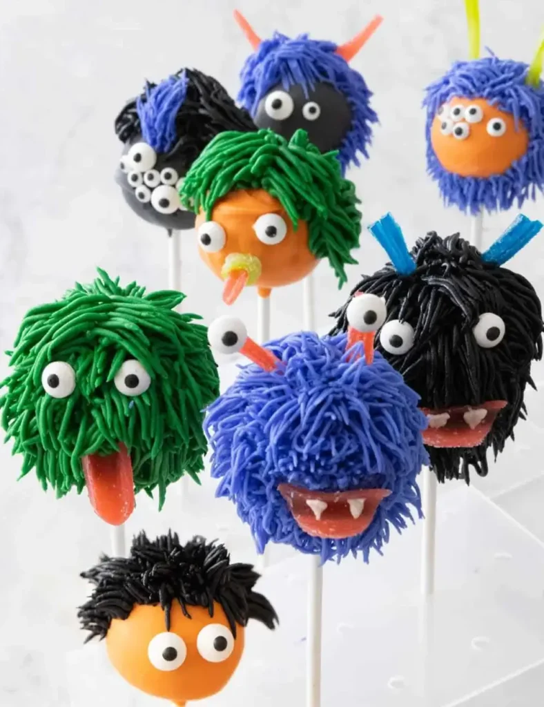 Colorful furry monster Halloween cake pops with candy eyes and fang mouths, displayed upright