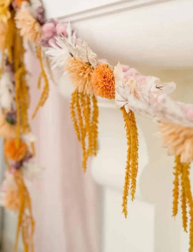 Fall floral garland made from faux leaves and flowers glued onto thick yarn, hanging across a mantel