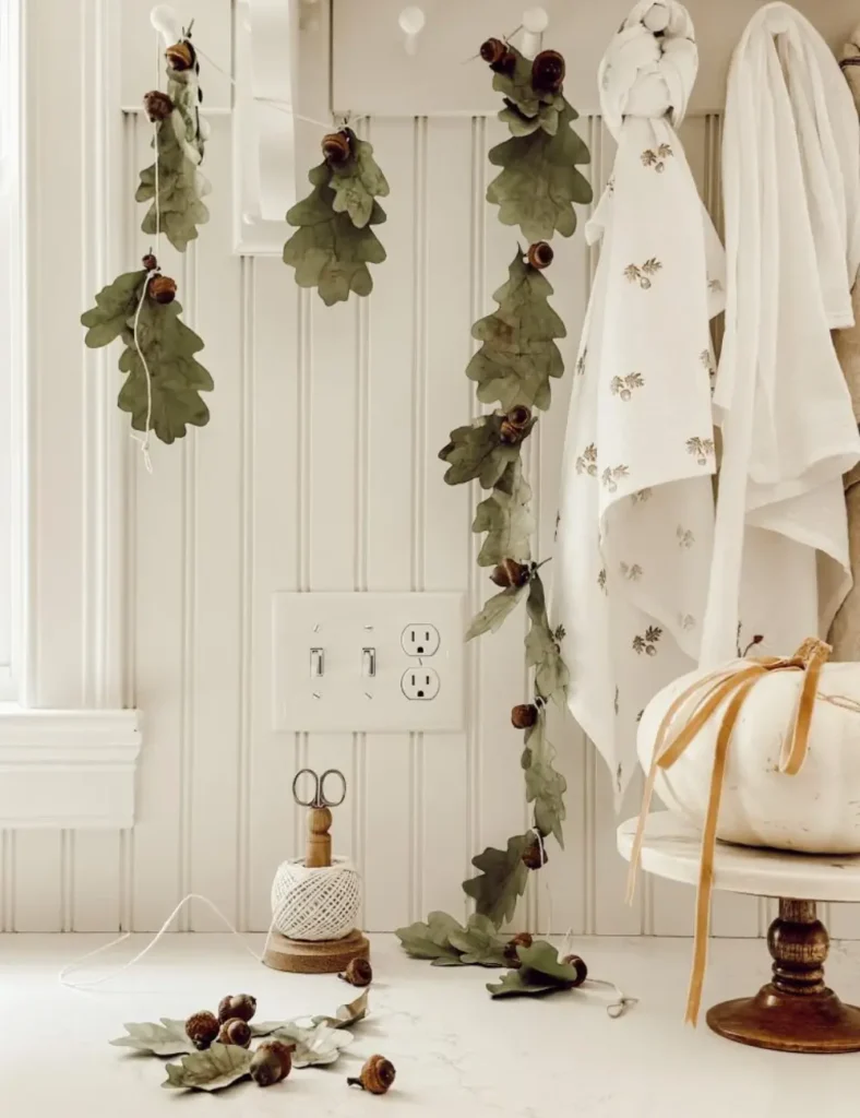 Fall garland of green paper oak leaves and real acorns tied along natural twine, hanging in a kitchen