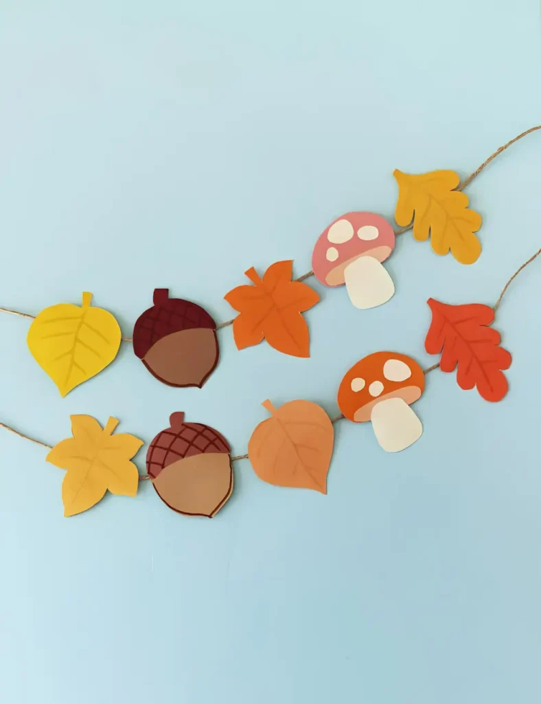 Fall paper garland with colorful paper leaves, acorns and spotted mushrooms hanging from a string on a wall