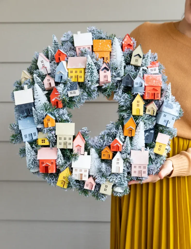Flocked Christmas wreath filled with colorful paper village houses and snowy bottle brush trees