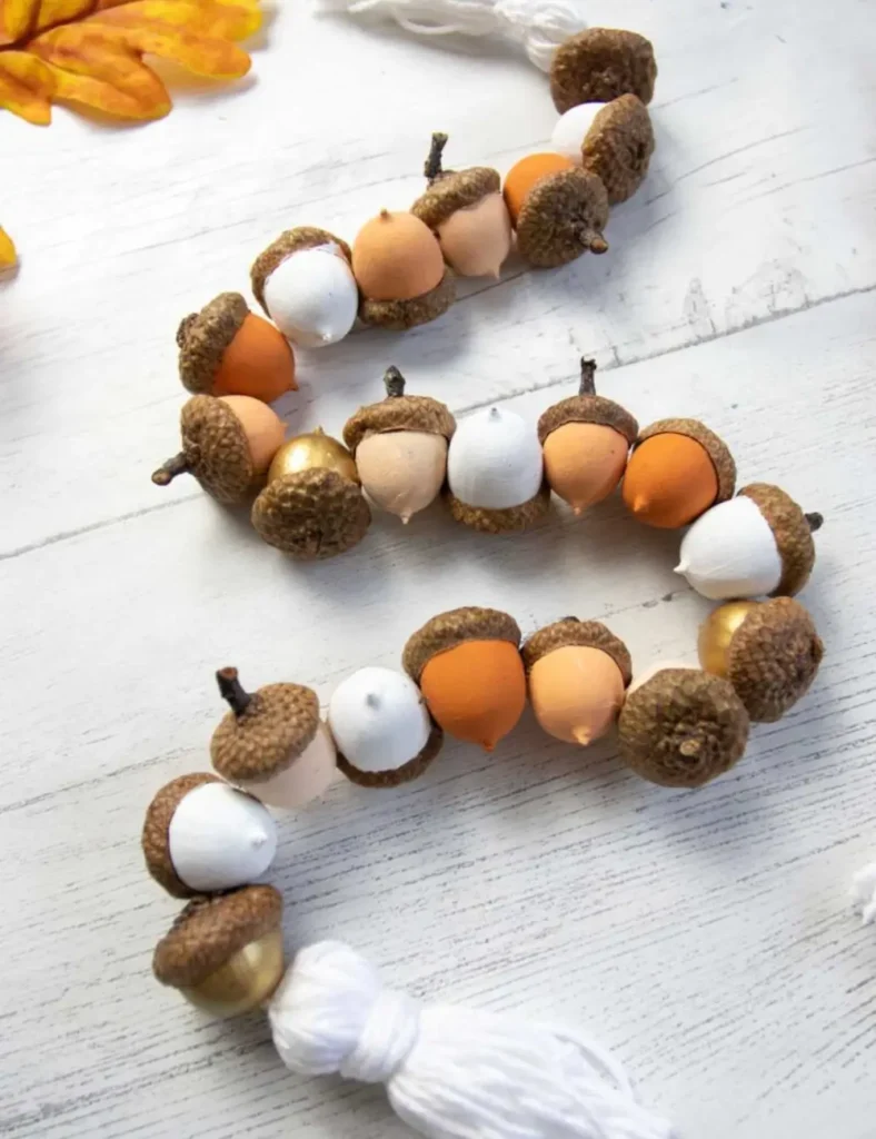 Garland of acorns with natural caps and orange and cream painted bottoms, strung on clear line with a tassel at the end