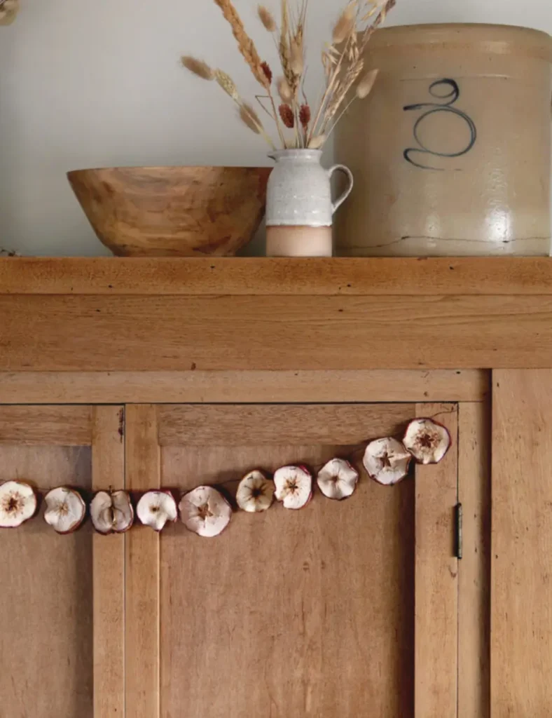 Garland of dried apple slices hanging on a wooden mantel with fall leaves and branches