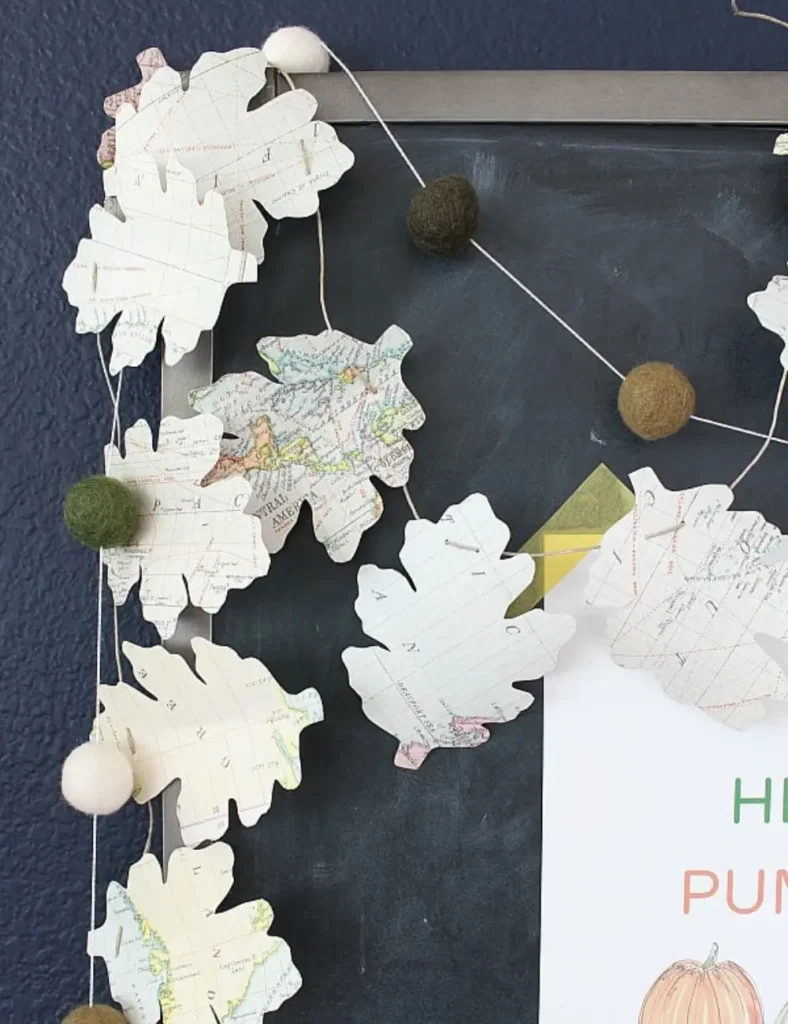 Garland of leaf shapes cut from a colorful world map, hung across a chalkboard with wool felt pom-poms nearby