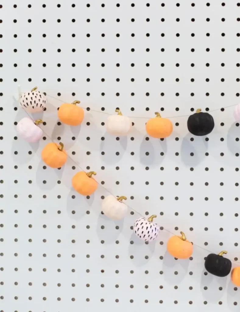 Garland of mini pumpkins painted black, white and blush pink with gold stems, strung on twine