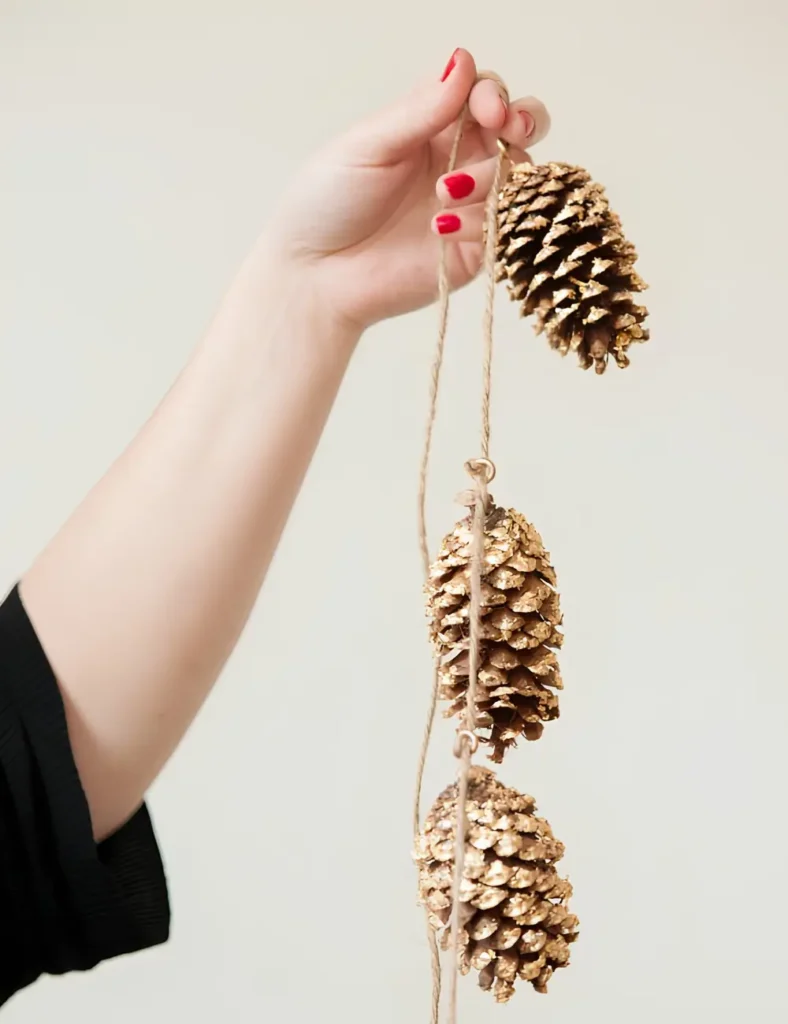 Garland of pine cones with gold leaf accents, strung on jute twine along a mantel
