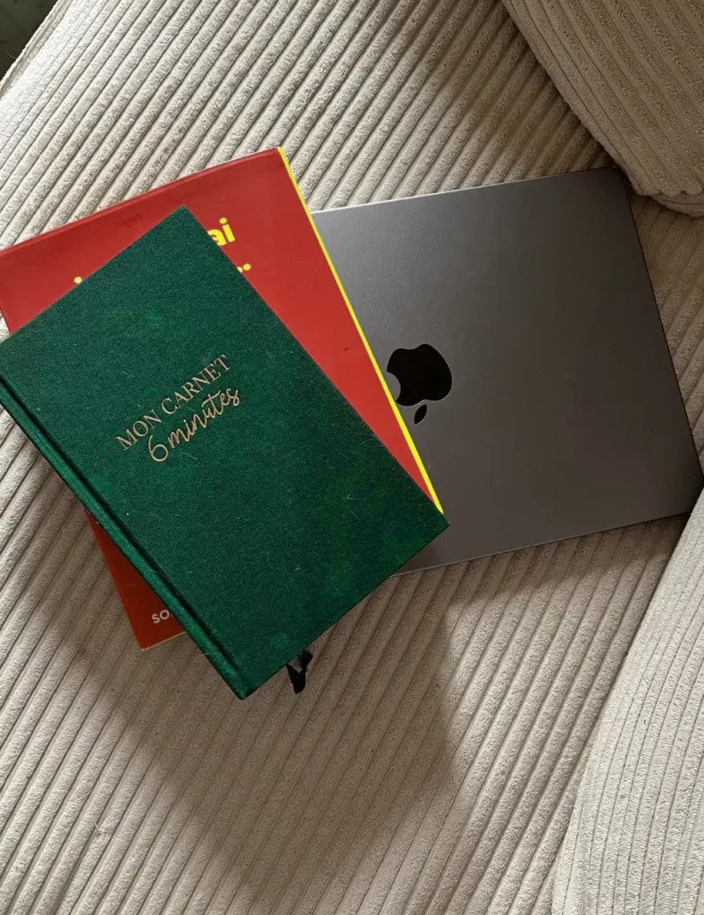 Green linen journal on a pink book and silver laptop on a cream corduroy sofa